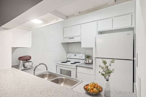 A kitchen with white appliances and a bowl of fruit on the counter.